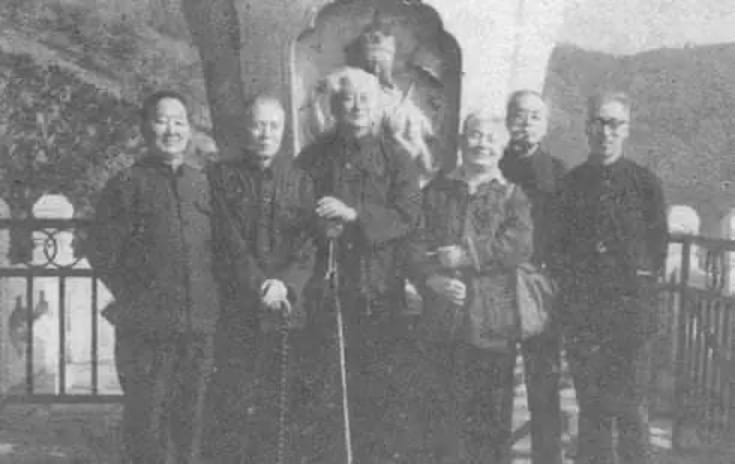Black and white photo of a group of men posing in front of what appears to possibly be a grave yard