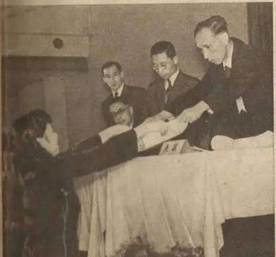 black and white image of a young women receiving an award from three men at a table