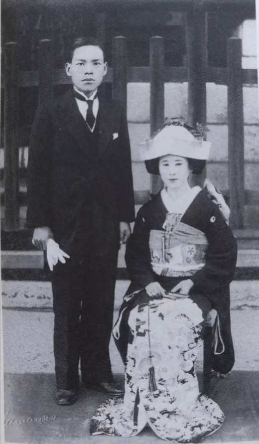 black and white photo of a man in a suit and a woman sitting down in traditional clothing